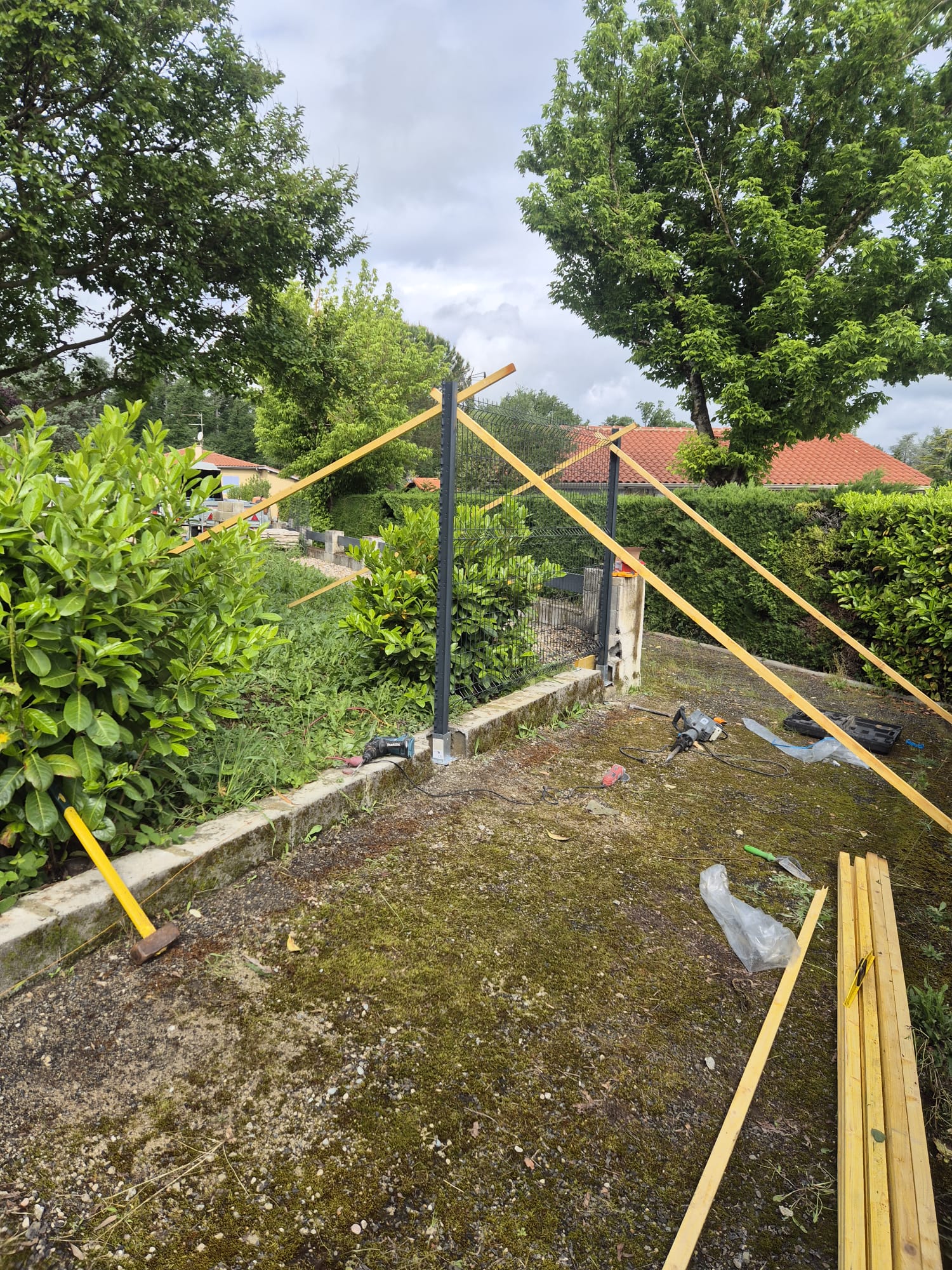 Pose des premiers poteaux métalliques de la clôture rigide sur le soubassement